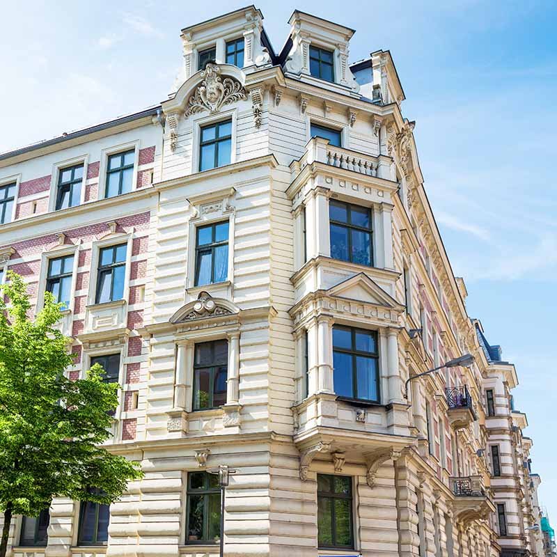 Mehrstöckiges Mehrfamilienhaus mit klassizistischer Fassade im Sonnenschein.